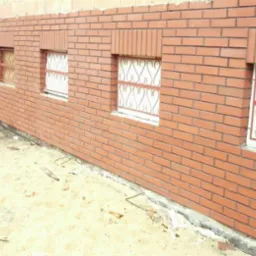 Ściana zewnętrzna z czerwonej cegły z czterema oknami z dekoracyjnymi, metalowymi kratami, widok z dołu.