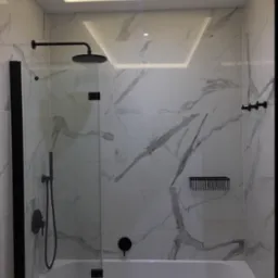 Nowoczesna łazienka z wanną i szklanym parawanem, wykończona białymi płytkami imitującymi marmur i czarną armaturą, oświetlenie sufitowe LED.