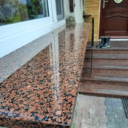 AgAd Bau - Polerowany, czerwono-czarny parapet z granitu na tle wejścia do domu z granitowymi schodami i butami roboczymi