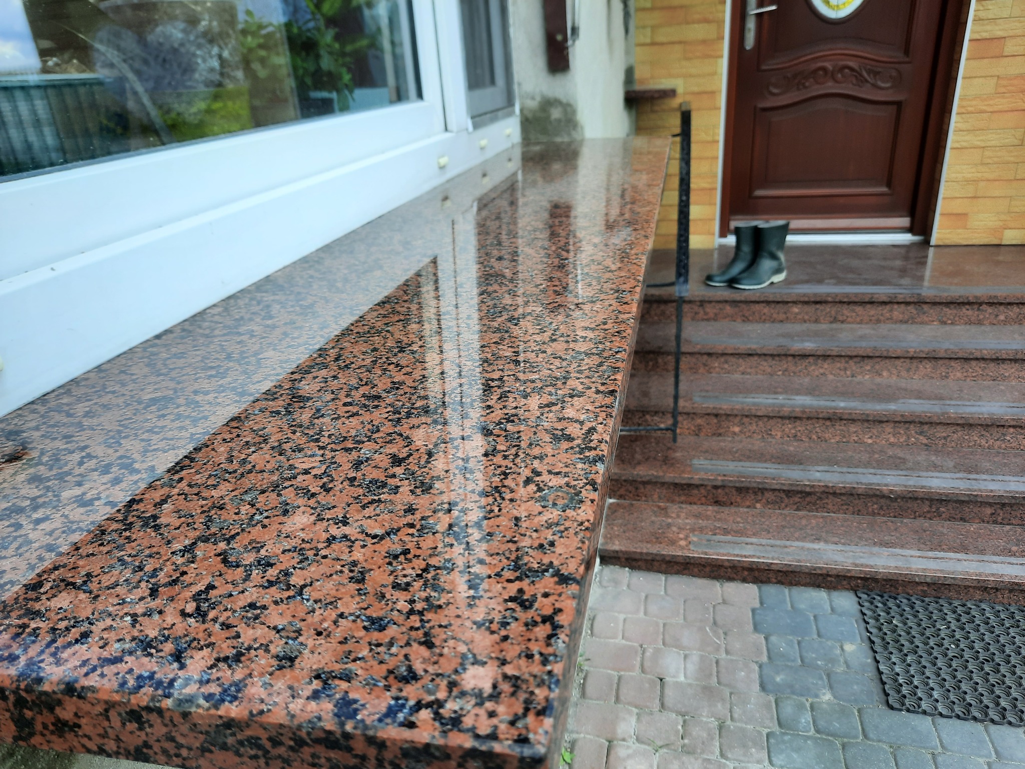 Polerowany, czerwono-czarny parapet z granitu na tle wejścia do domu z granitowymi schodami i butami roboczymi