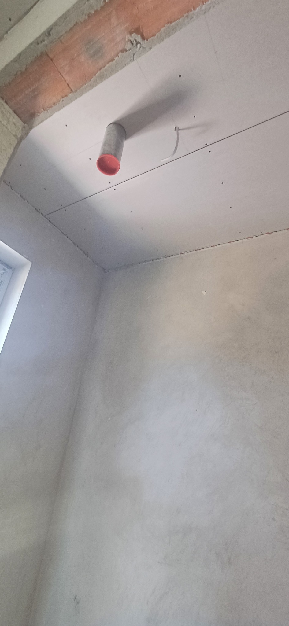 Wnętrze w trakcie remontu: ściany po szpachlowaniu, sufit z płyt karton-gips z wystającym elementem instalacji. Widoczne łączenia płyt gipsowych.