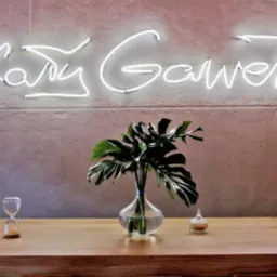 Wnętrze biura we Wrocławiu z neonowym napisem na ścianie, monstera w szklanym wazonie, klepsydra i mały słoiczek na drewnianym blacie.