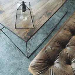 Stylowy stolik kawowy z ciemnego drewna z metalową podstawą i dekoracyjną lampą w kształcie klatki, obok skórzany puf z guzikami, widok z góry.