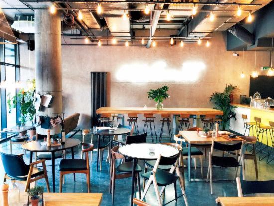 Wnętrze kawiarni w stylu industrialnym z surowymi ścianami, betonowym filarem, podwieszonymi lampami i różnymi rodzajami stolików i krzeseł.