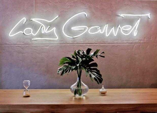 Wnętrze biura we Wrocławiu z neonowym napisem na ścianie, monstera w szklanym wazonie, klepsydra i mały słoiczek na drewnianym blacie.