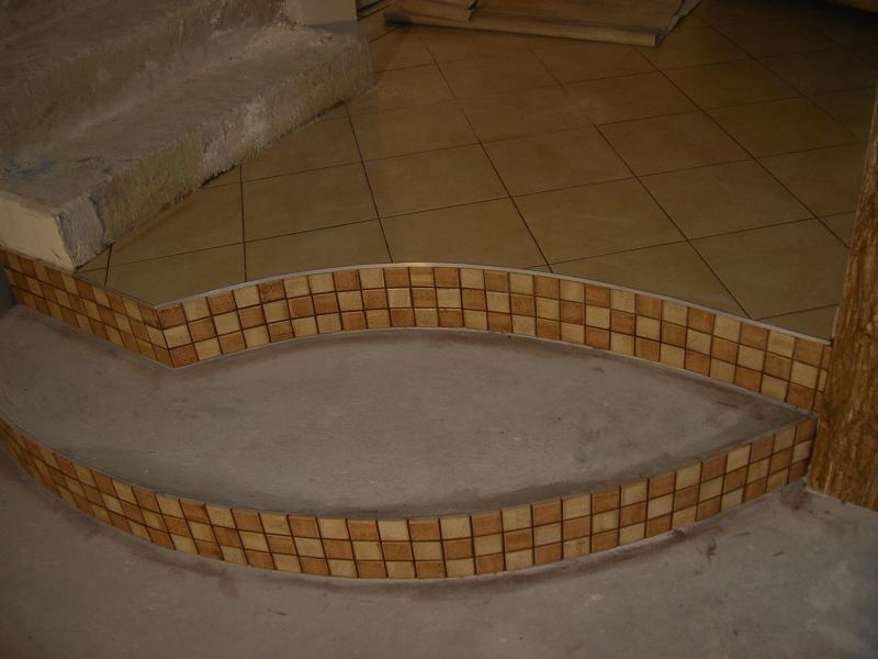 Niedokończone schody betonowe z wykończeniem z mozaiki w odcieniach brązu i beżu, widoczne płytki podłogowe w tle.