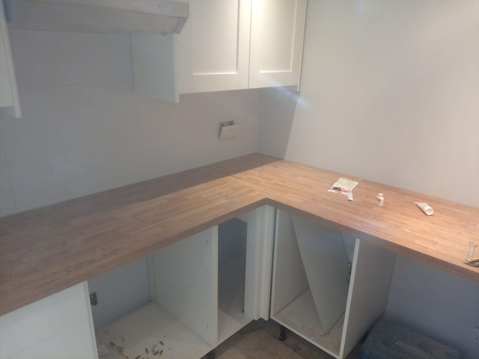 Montaż drewnianego blatu kuchennego w nowej zabudowie, widoczne białe szafki bez frontów i akcesoria montażowe na blacie.