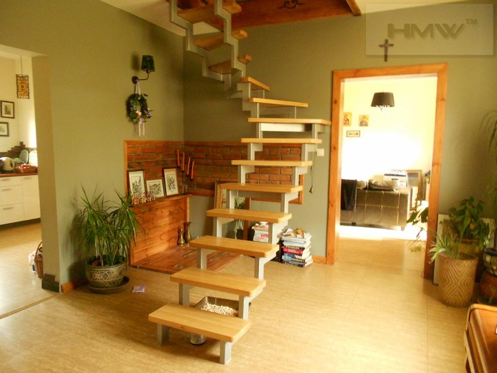 Nowoczesne schody drewniane z metalową konstrukcją w jasnym wnętrzu domu, widoczne elementy dekoracyjne z cegły i rośliny doniczkowe.