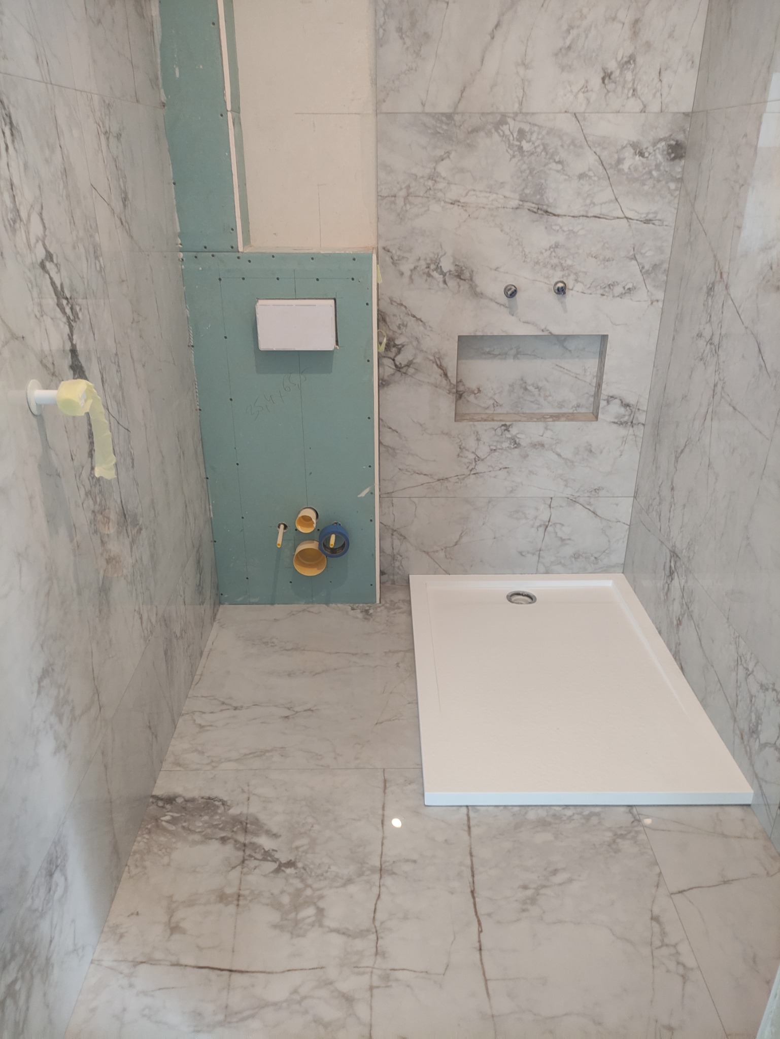 Montaż instalacji podtynkowych w łazience z marmurowymi płytkami, widoczny stelaż podtynkowy, odpływ liniowy i przygotowane podejścia wodno-kanalizacyjne.