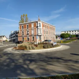 Trzypiętrowy budynek z czerwonej cegły z białymi akcentami, widziany z ronda w słoneczny dzień.