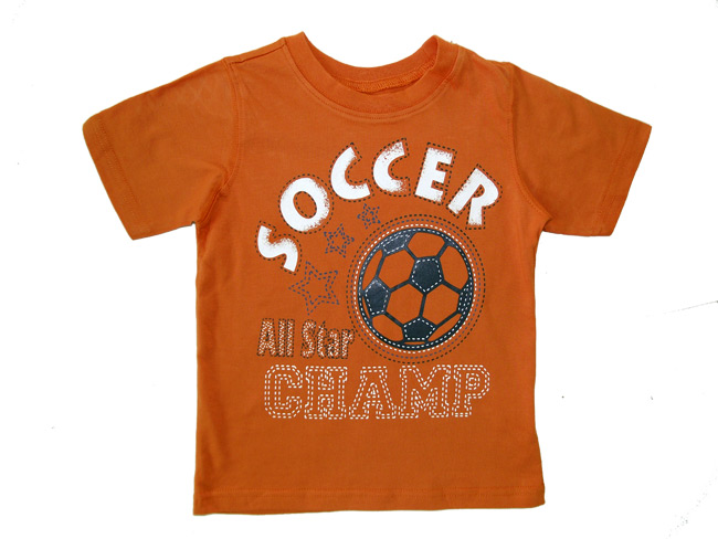 Pomarańczowa koszulka dziecięca z nadrukiem piłki nożnej, napisem 'SOCCER All Star CHAMP' i dekoracyjnymi gwiazdkami, leżąca na białym tle.