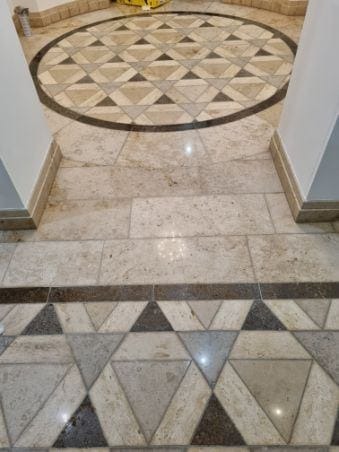 Beżowa posadzka kamienna z dekoracyjnym wzorem trójkątów i okręgiem w centrum, widok z góry na wykończone wnętrze. Detal wykończenia podłogi.
