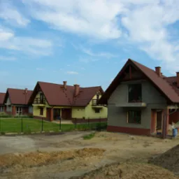 Rząd nowych domów jednorodzinnych z brązowymi dachami w trakcie budowy, widoczne fragmenty elewacji i przygotowane podłoże.