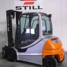 Wózek widłowy STILL RX 60-40 w srebrno-pomarańczowej kolorystyce, z kabiną i czarnymi oponami, na tle białej ściany z logo producenta i wyświetlaczem.