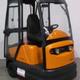 Pomarańczowo-czarny wózek elektryczny STILL R06 z kabiną, widoczny z przodu, na tle jasnej ściany. Na maszynie widoczna naklejka z logo STILL.