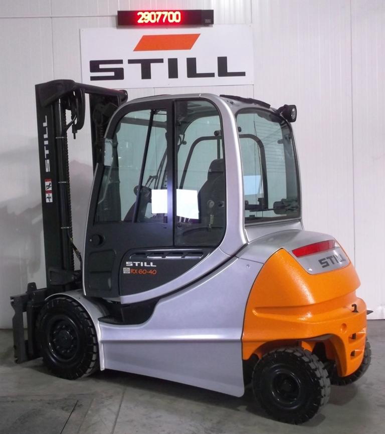 Wózek widłowy STILL RX 60-40 w srebrno-pomarańczowej kolorystyce, z kabiną i czarnymi oponami, na tle białej ściany z logo producenta i wyświetlaczem.