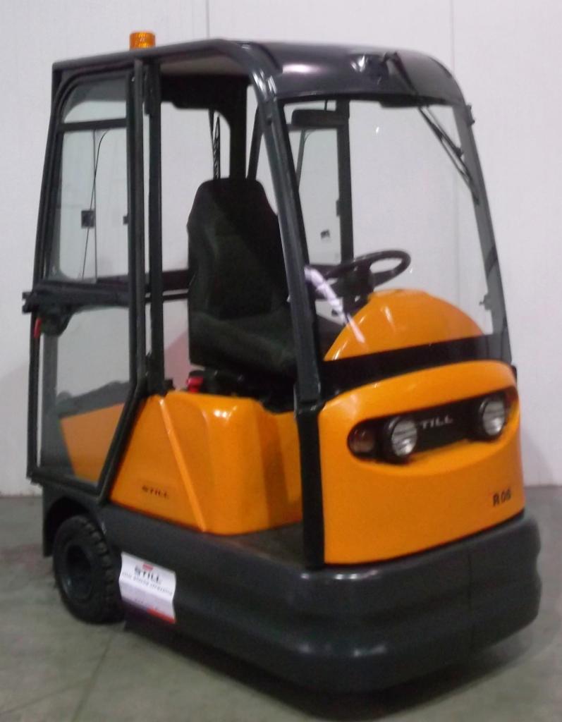 Pomarańczowo-czarny wózek elektryczny STILL R06 z kabiną, widoczny z przodu, na tle jasnej ściany. Na maszynie widoczna naklejka z logo STILL.