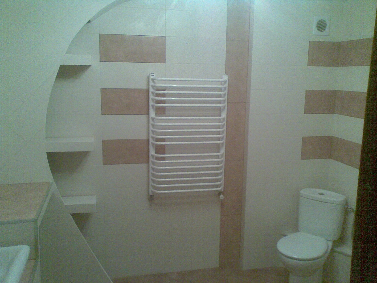 Ukończona łazienka z jasnymi płytkami w poziome pasy, biała toaleta i grzejnik drabinkowy.