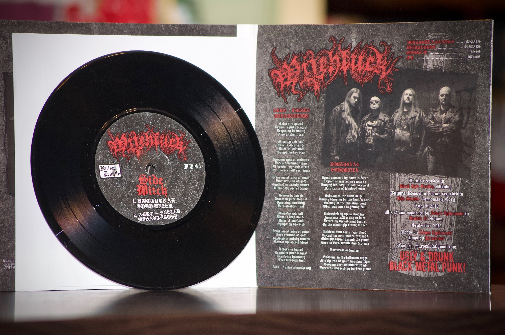 Czarna płyta winylowa z okładką albumu death metalowego zespołu, widoczne nazwy utworów 'Nocturnal Sodomizer' i 'Alko-Fueled Misanthropy', obok okładka z nazwą zespołu i zdjęciem muzyków.