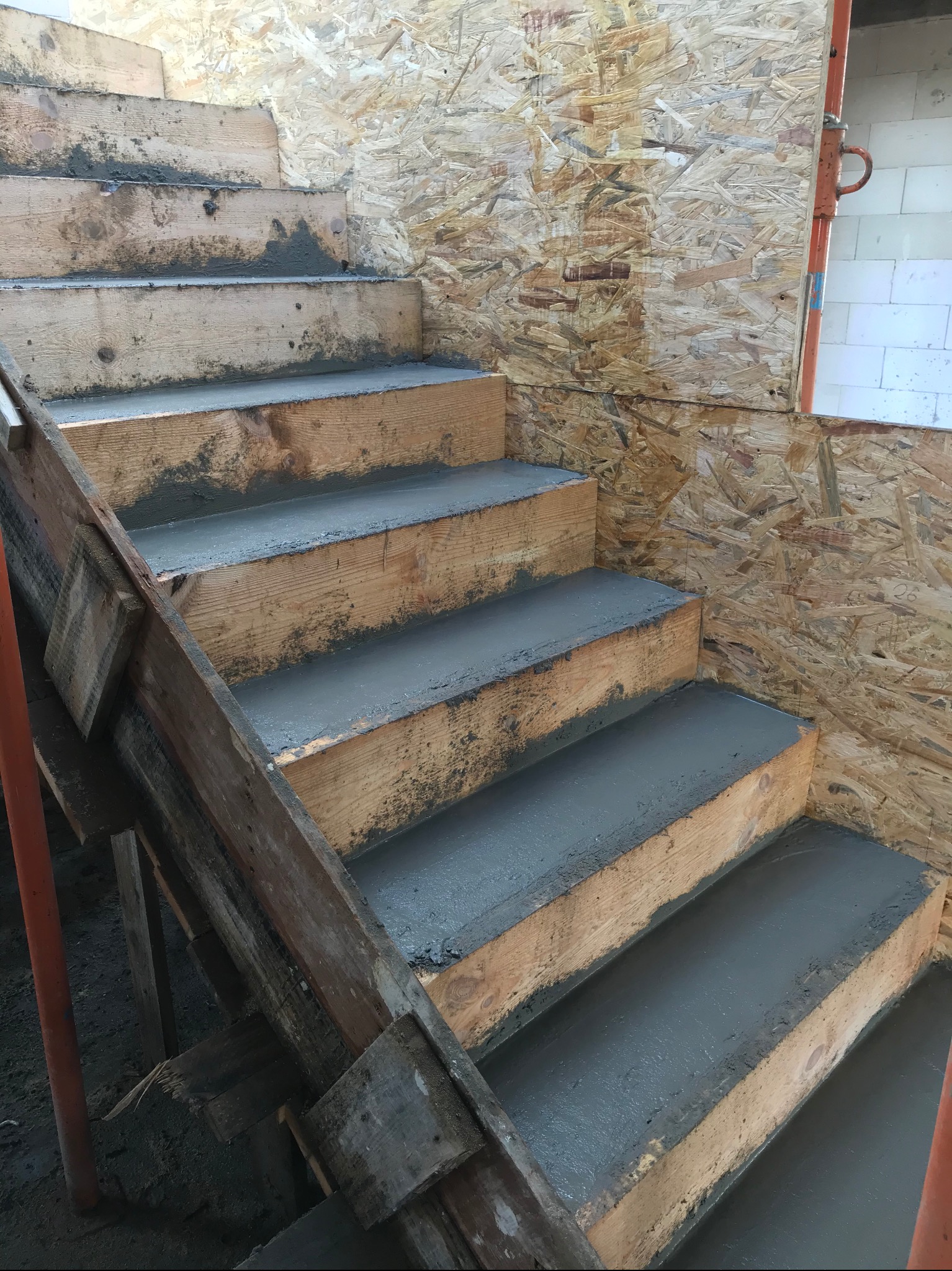 Surowe, drewniane schody w trakcie betonowania, widoczne szalunki i płyta OSB na ścianie.