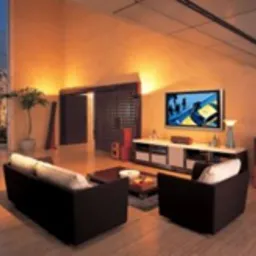 Nowoczesne wnętrze salonu z systemem nagłośnienia: ciemne sofy i fotele, telewizor na szafce RTV, wysokie okna z widokiem na zewnątrz, oraz kolumny głośnikowe w kolorze czerwonego wina...