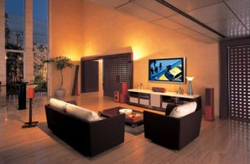 Nowoczesne wnętrze salonu z systemem nagłośnienia: ciemne sofy i fotele, telewizor na szafce RTV, wysokie okna z widokiem na zewnątrz, oraz kolumny głośnikowe w kolorze czerwonego wina...