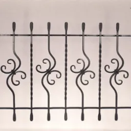 Kute, metalowe ogrodzenie z dekoracyjnymi elementami w kształcie czterolistnych koniczynek, zwieńczone ozdobnymi grotami, w czarno-białej tonacji.