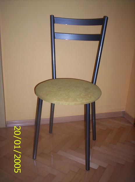 Metalowy krzesło z okrągłym, żółtym siedziskiem na tle pomarańczowej ściany i parkietu.