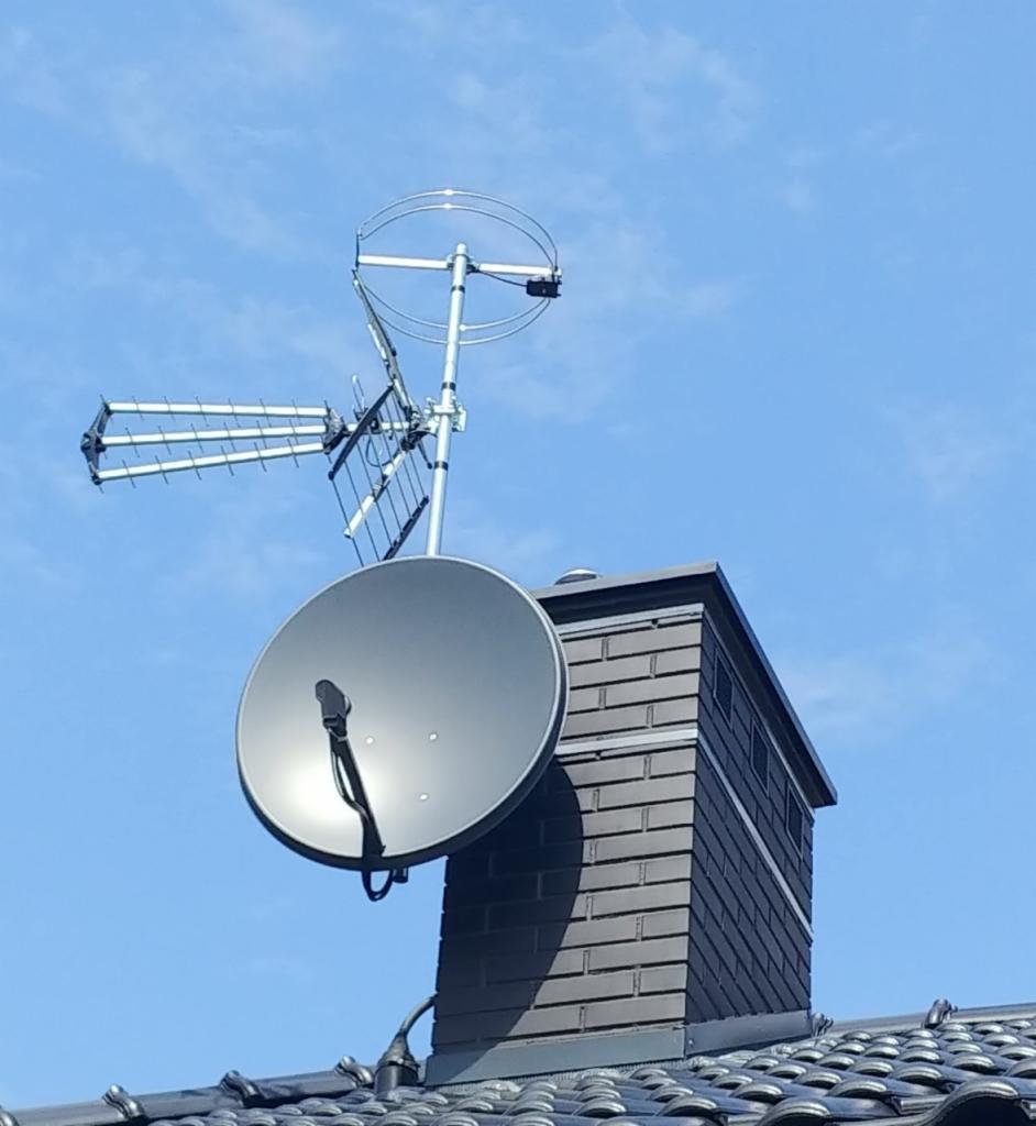 Antena satelitarna i antena naziemna zamontowane na kominie z cegły na dachu pokrytym dachówką, widok w pogodny dzień.
