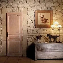 Ściana wyłożona kamieniem dekoracyjnym z drewnianą, jasną ramą drzwi, obrazem z motywem kaczek i komodą z lampkami w rustykalnym stylu.