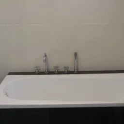 Biała wanna obudowana czarnymi płytkami, z chromowaną armaturą na tle jasnobeżowych płytek ściennych.