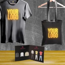 Prezentacja odzieży i torby z nadrukowanym logo, widoczna broszura z kolekcją ubrań na drewnianym tle.