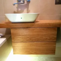 Nowoczesna łazienka z umywalką nablatową na drewnianym blacie z szufladami, podświetlona od dołu, z widoczną armaturą chromowaną i fragmentem wanny.