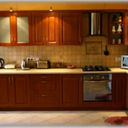 Kompletna zabudowa kuchenna z drewnianymi frontami w odcieniu ciepłego brązu, z blatem w jasnym kolorze, wyposażona w sprzęt AGD, widoczna z perspektywy szerokokątnej.