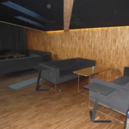 Wnętrze z drewnianą ścianą, szarymi sofami i stolikami pomocniczymi, podłoga imitująca drewno, widoczne elementy oświetlenia sufitowego.