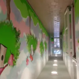Długi korytarz z bajkowymi malowidłami na ścianach, przedstawiającymi drzewa i domki dla ptaków. Światło pada z okien i lamp podłogowych.