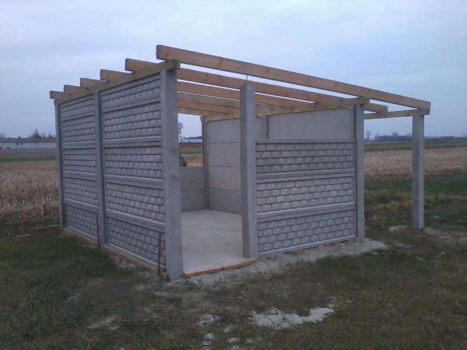 Wznoszona wiata z prefabrykatów betonowych z drewnianą konstrukcją dachu na polu uprawnym.