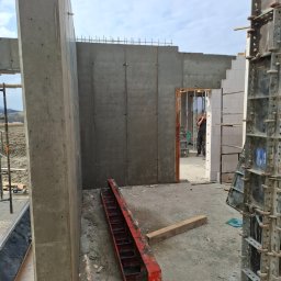 Przemysław Pytel - Surowy stan budowy domu z betonu: ściany szalunkowe, zbrojenia, widoczne elementy konstrukcyjne i pracownik w tle. Wnętrze budynku w trakcie wznoszenia.