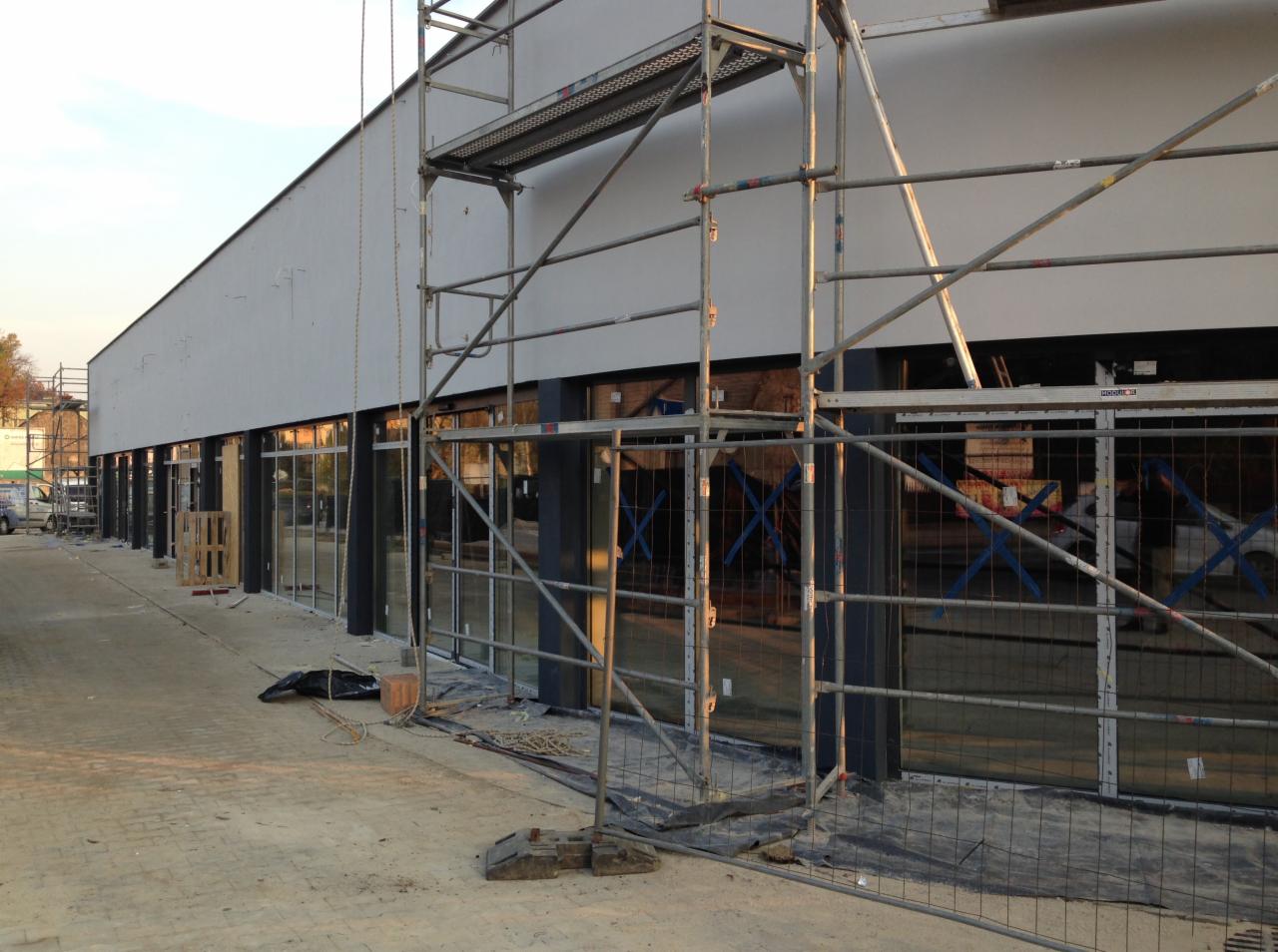 Montaż okien w nowym budynku, widoczne rusztowania i zabezpieczenia budowlane, surowy stan wykończenia.