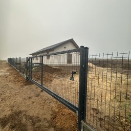 MAR-BET Ogrodzenia Czujak - Nowoczesne ogrodzenie panelowe z przesuwną bramą wjazdową, widoczne narzędzie montażowe, dom w tle, pochmurny dzień. Solidna konstrukcja, estetyczne wykończenie.
