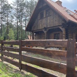 MAR-BET Ogrodzenia Czujak - Rustykalne, drewniane ogrodzenie posesji z bali, na tle domu z bali i zieleni. Widoczne naturalne wykończenie drewna i dopasowanie do otoczenia.