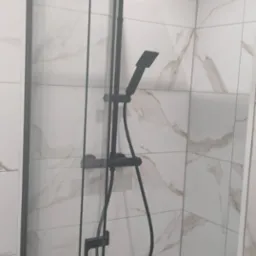 Nowoczesna kabina prysznicowa z czarną armaturą, deszczownicą i słuchawką, wyłożona płytkami imitującymi marmur.