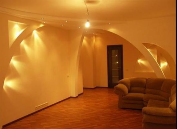 Jasne wnętrze z parkietem, oświetleniem punktowym i dekoracyjnymi wnękami w ścianach, sofa w odcieniach brązu