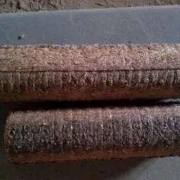 Dwa cylindryczne kawałki sprasowanego materiału opałowego, ułożone jeden na drugim, z widoczną teksturą włókien i śladami sprasowania.