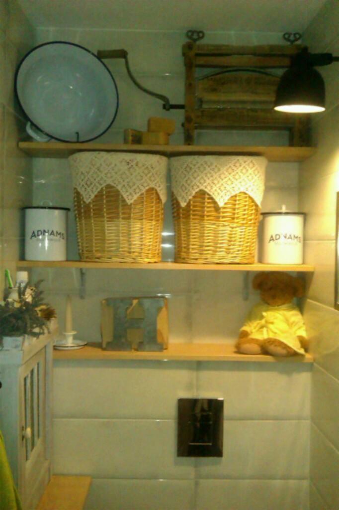 Półki z dekoracjami w łazience w Bydgoszczy: emaliowana misa, pralka ręczna, wiklinowe kosze z koronką, puszki z napisem i pluszowy miś w żółtej sukience.
