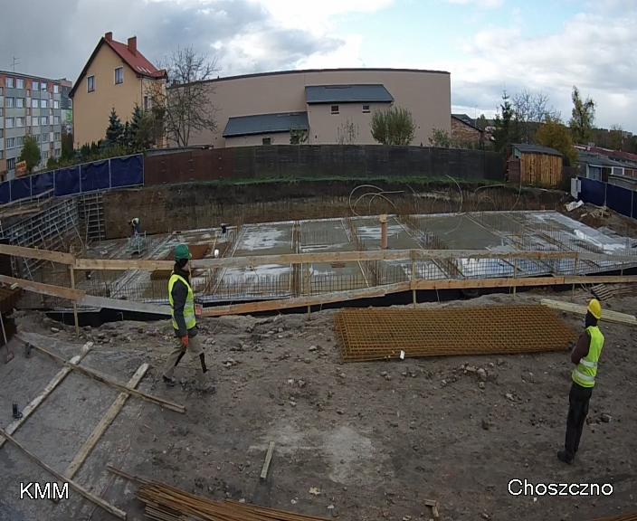 Fundamenty domu jednorodzinnego w Recz, widok z góry na zbrojenie, szalunki i częściowo wylany beton. Pracownicy w kamizelkach odblaskowych na placu budowy.