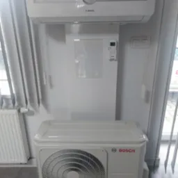 Klimatyzator Bosch typu split, jednostka wewnętrzna i zewnętrzna, zamontowany na białej ścianie, widoczny pilot sterowania.