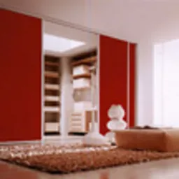 Wnętrze garderoby z narożną zabudową, z przesuwnymi drzwiami w kolorze intensywnej czerwieni, widoczny system półek i szuflad, na pierwszym planie pufa i dywan z długim włosiem w odcieniach brązu.