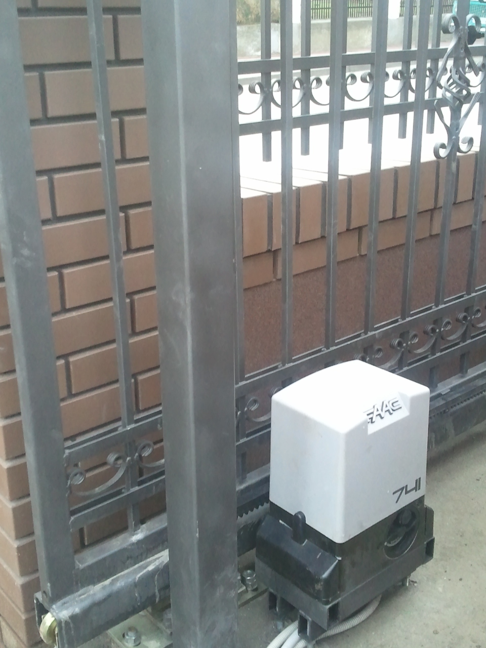 Automat FAAC 741 zainstalowany przy metalowej, ozdobnej bramie przesuwnej z ceglanym słupkiem.