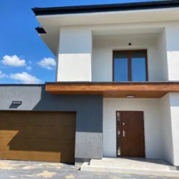 Nowoczesny dom jednorodzinny z drewnianą bramą garażową i drzwiami wejściowymi, oświetlenie zewnętrzne, elewacja w kolorze białym i szarym, błękitne niebo.